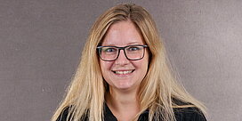 Portrait der Büro-Mitarbeiterin Katja Seip vor grauem Hintergrund.