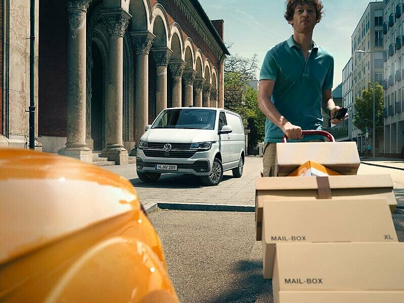 Transporter 6.1 für Kurier und Logistik: Mann mit Postboxen liefert aus.