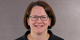 Portrait der Büro-Mitarbeiterin Andrea Trautmann vor grauem Hintergrund.