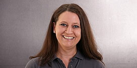 Portrait der Servicemitarbeiterin Ramona Stockert vor grauem Hintergrund.