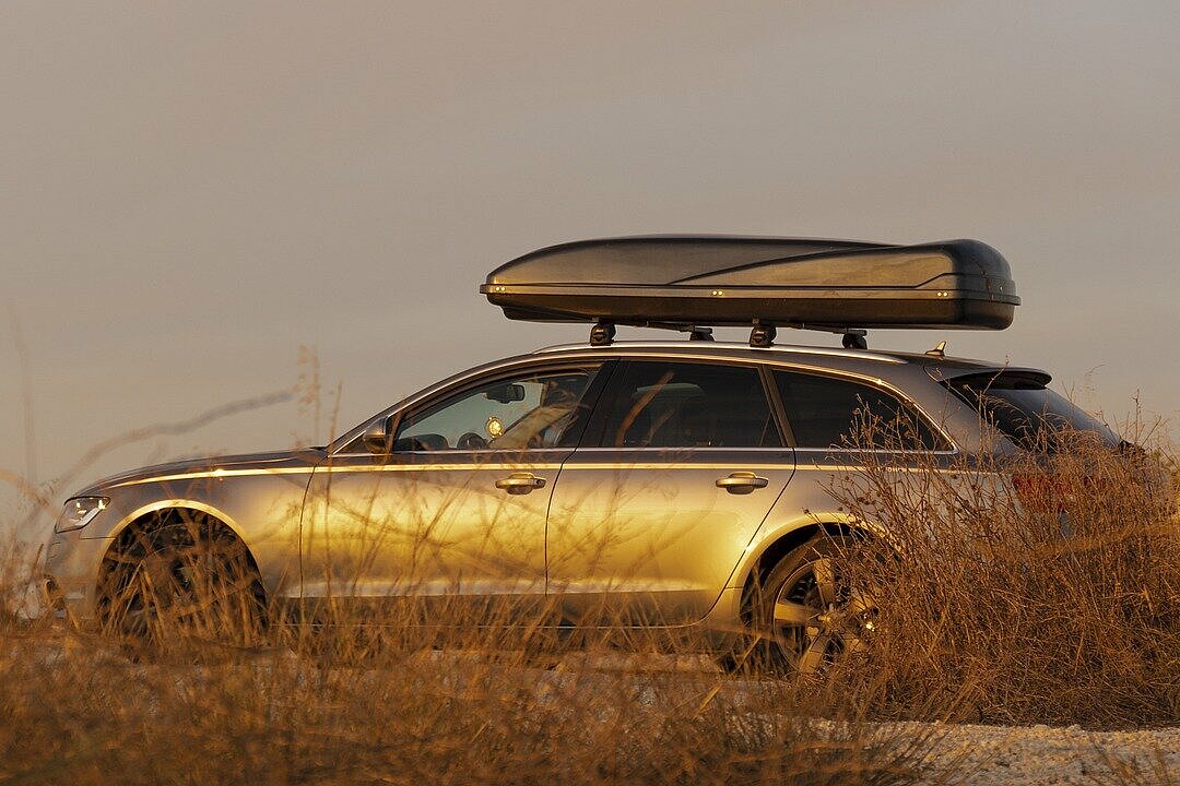 Audi Pkw mit Dachbox in Dünenlandschaft im Sonnenuntergang.