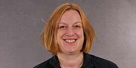 Portrait der Büromitarbeiterin Christine Heldmann vor grauem Hintergrund.