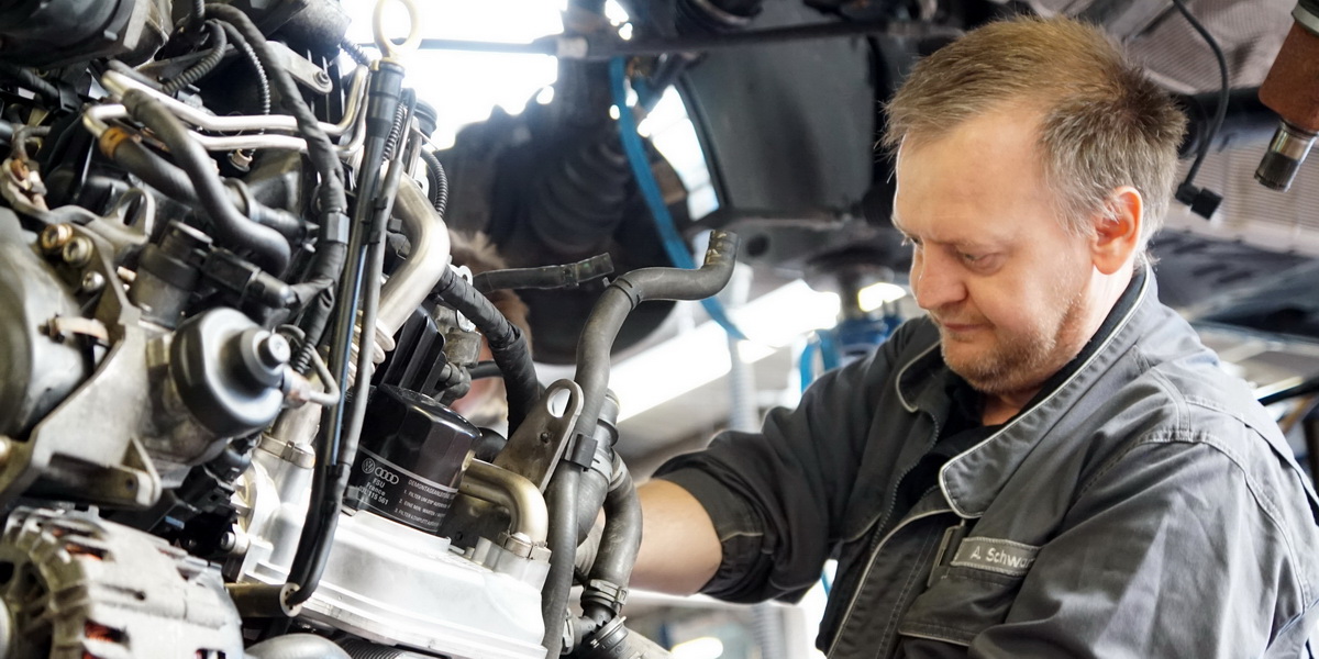 Kfz-Mechatroniker arbeitet an einem ausgebauten Auto Motor in der Werkstatt. 